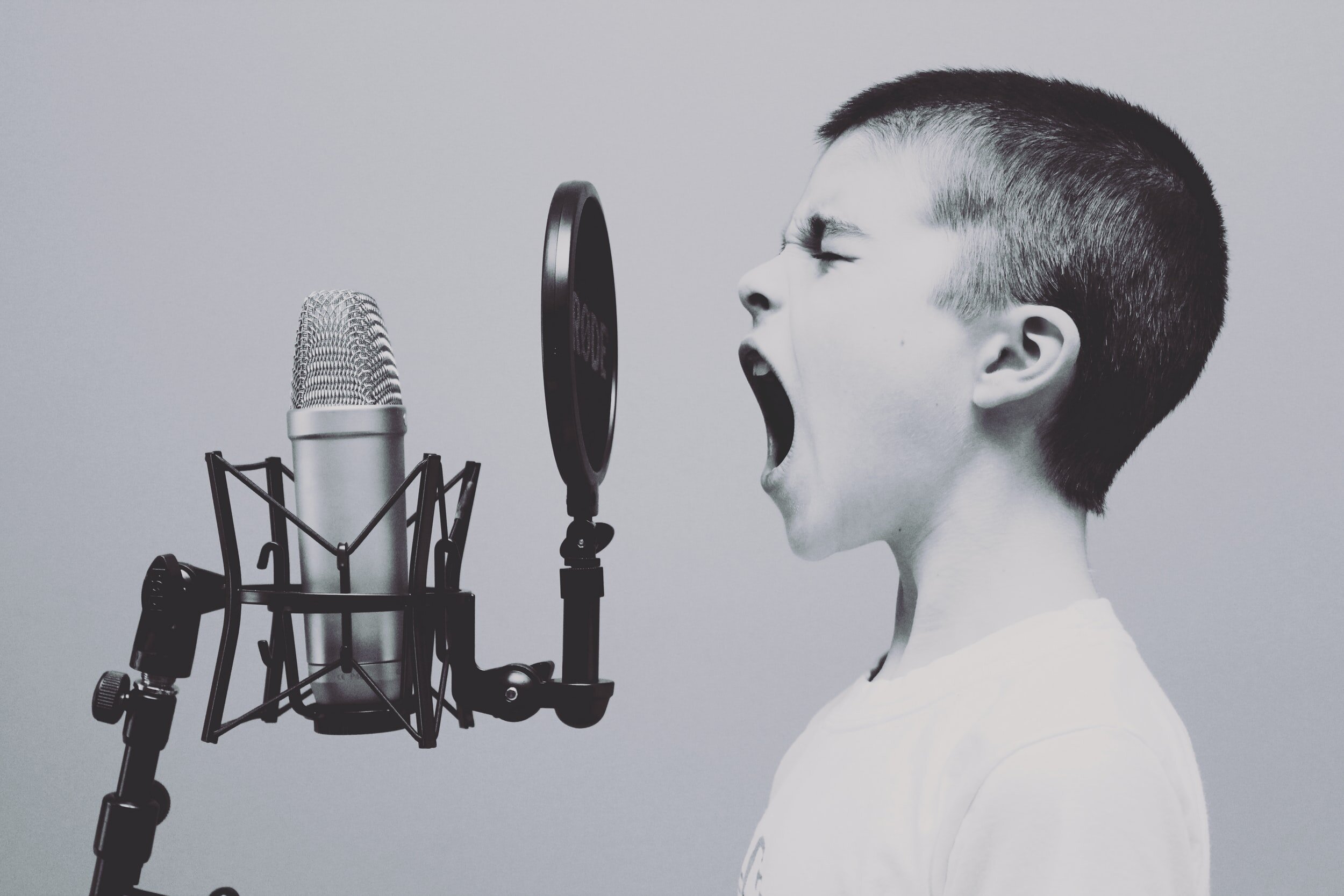 A boy shouting into a studio microphone with a pop filter