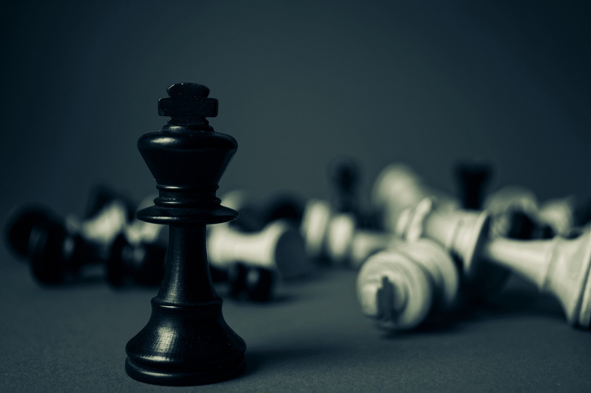 A black king chess piece standing upright while other pieces lie toppled in the background