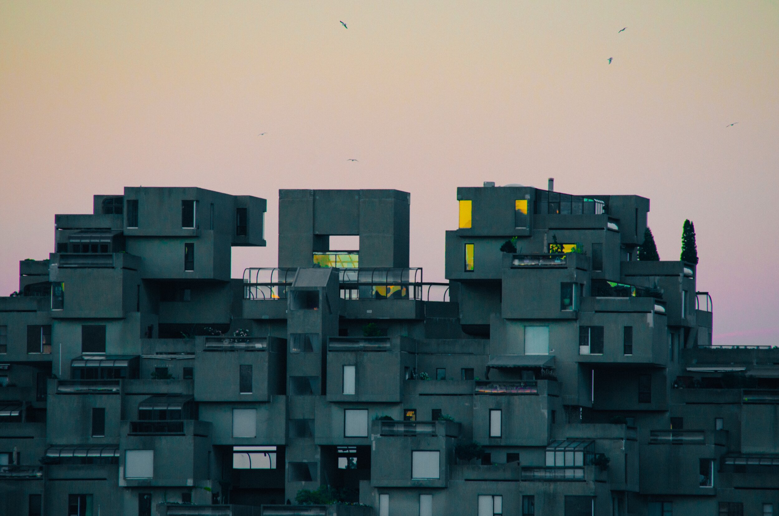Habitat 67&rsquo;s stacked modular apartment blocks in Montreal at dusk, with birds flying overhead