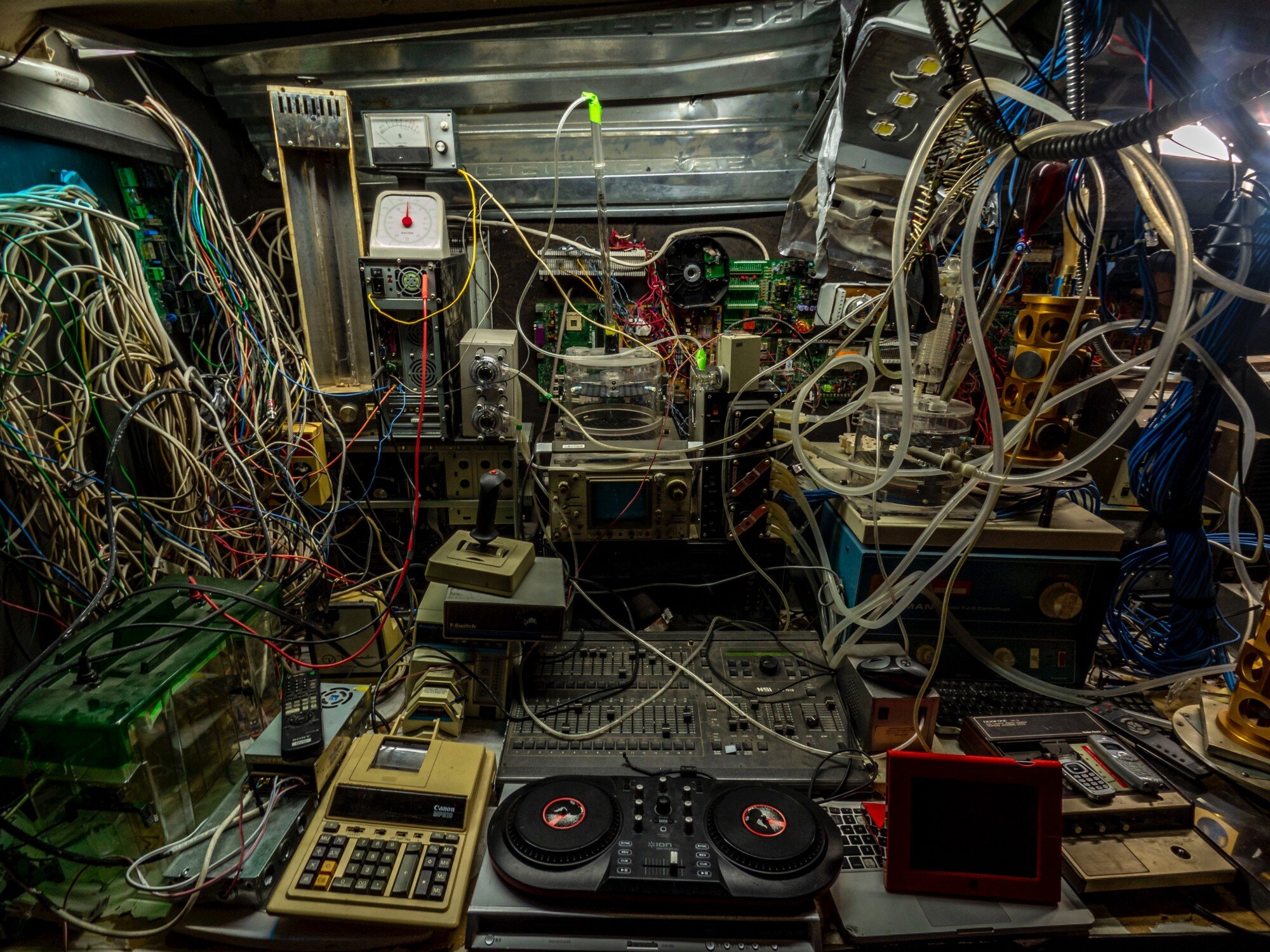 A cluttered tangle of wires, circuit boards, and outdated electronics crammed into a workshop
