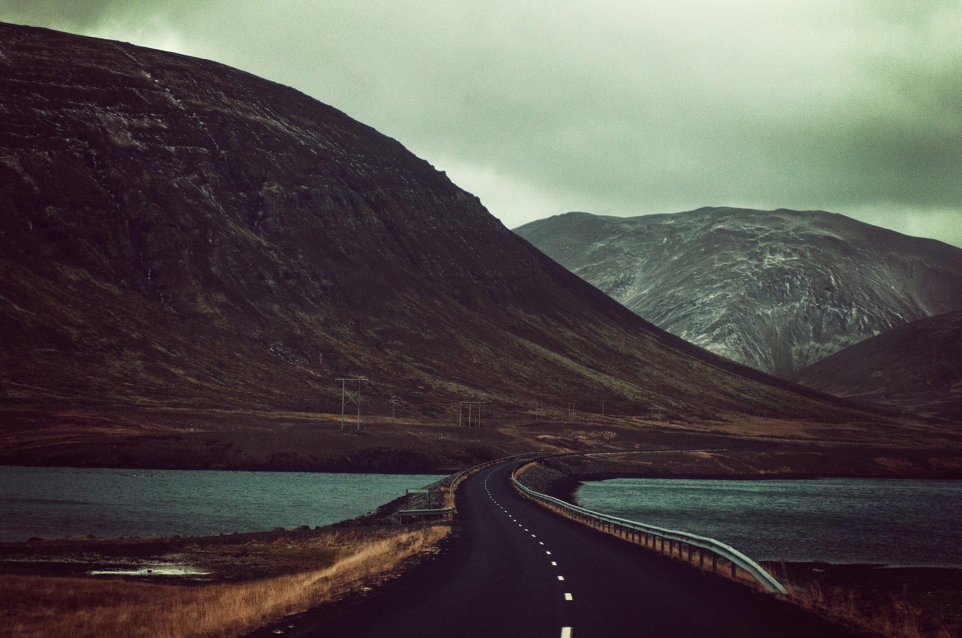 A paved road winding between two lakes toward misty mountains