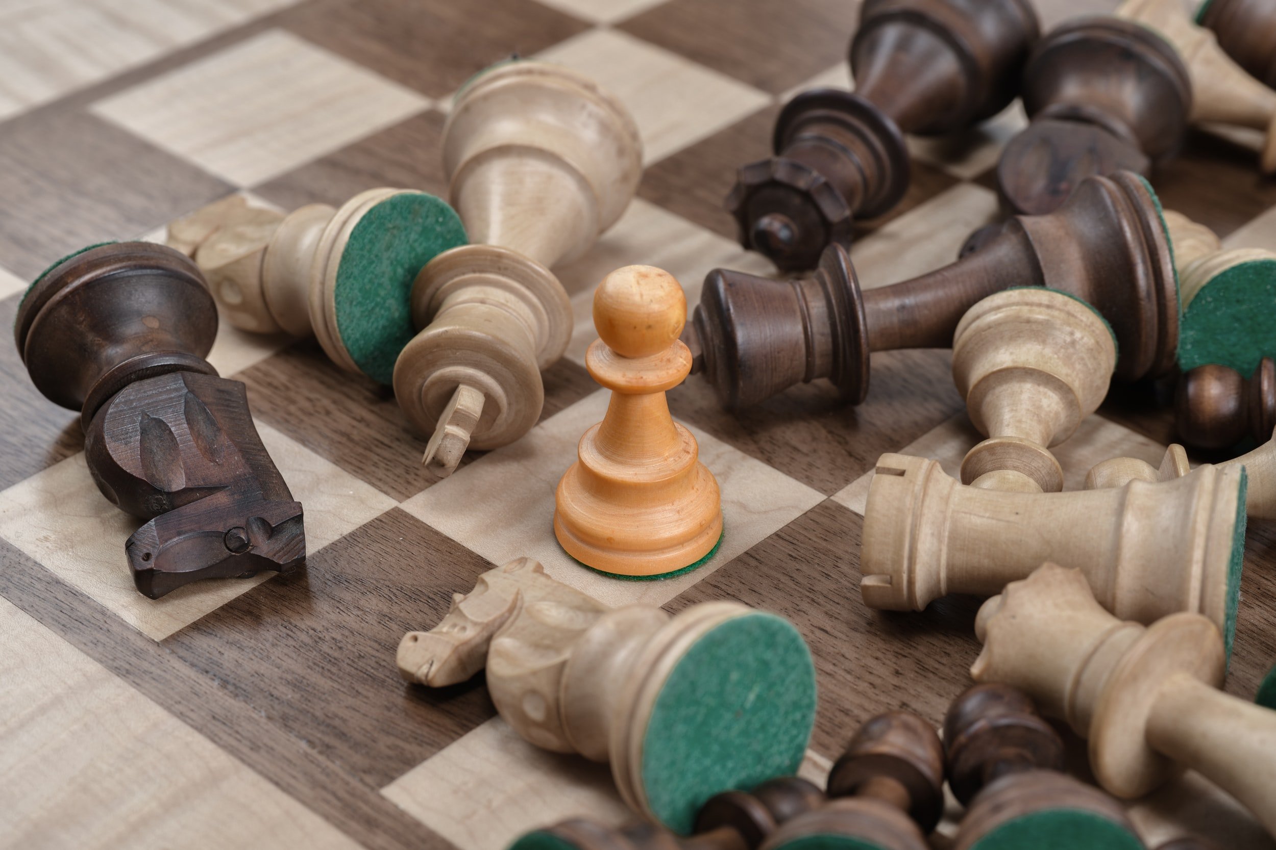 A single standing pawn surrounded by toppled chess pieces