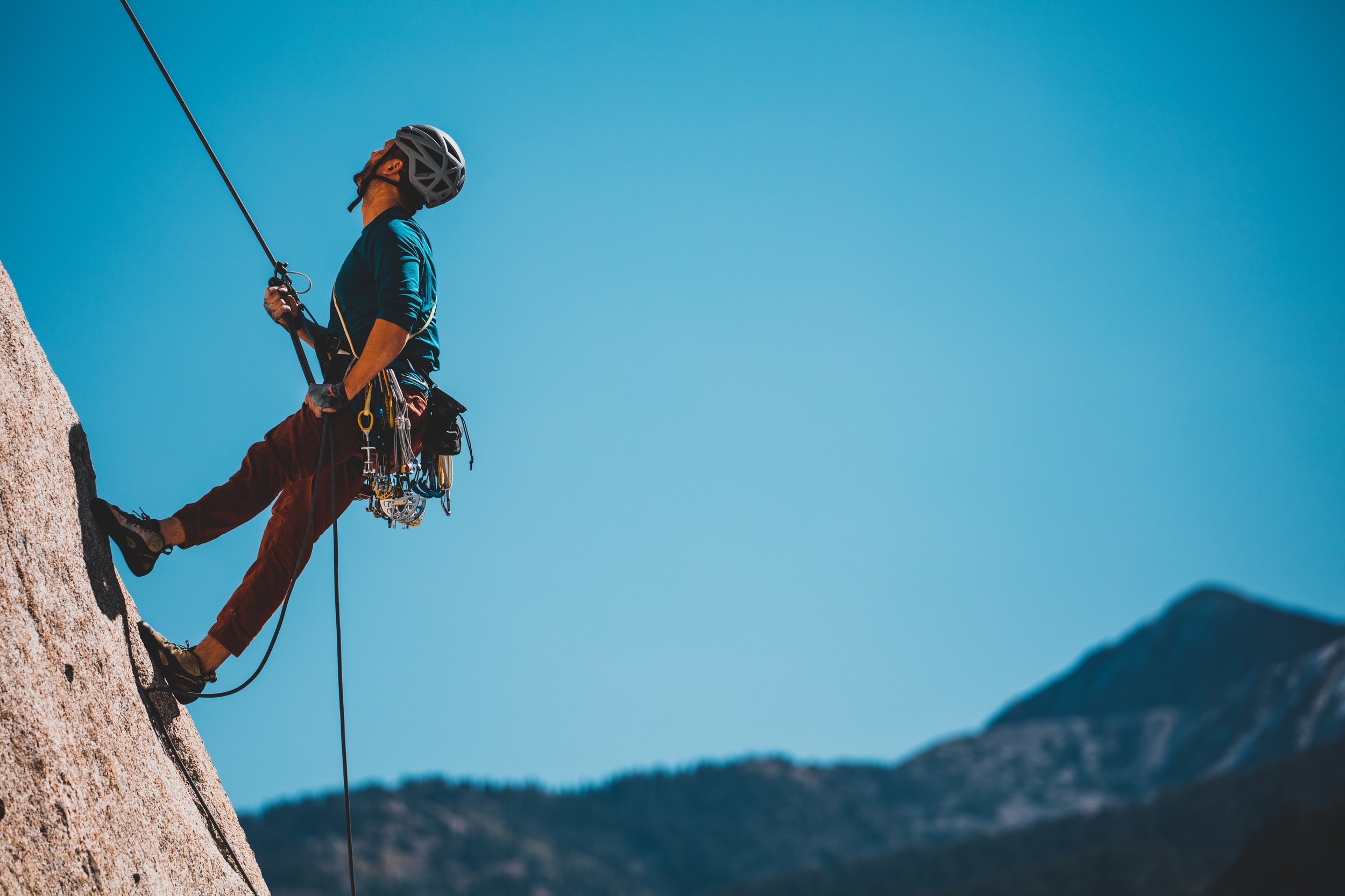 A climber rappelling down a rock face with mountains in the background